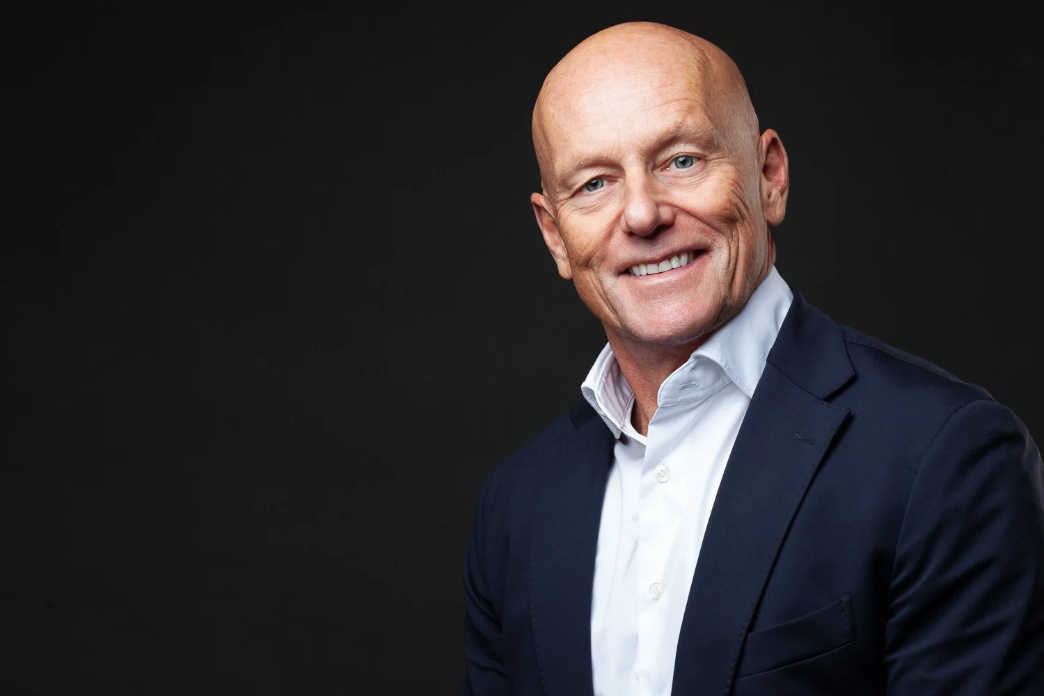 Older man with a warm smile, navy blazer, executive headshot London against a dark background