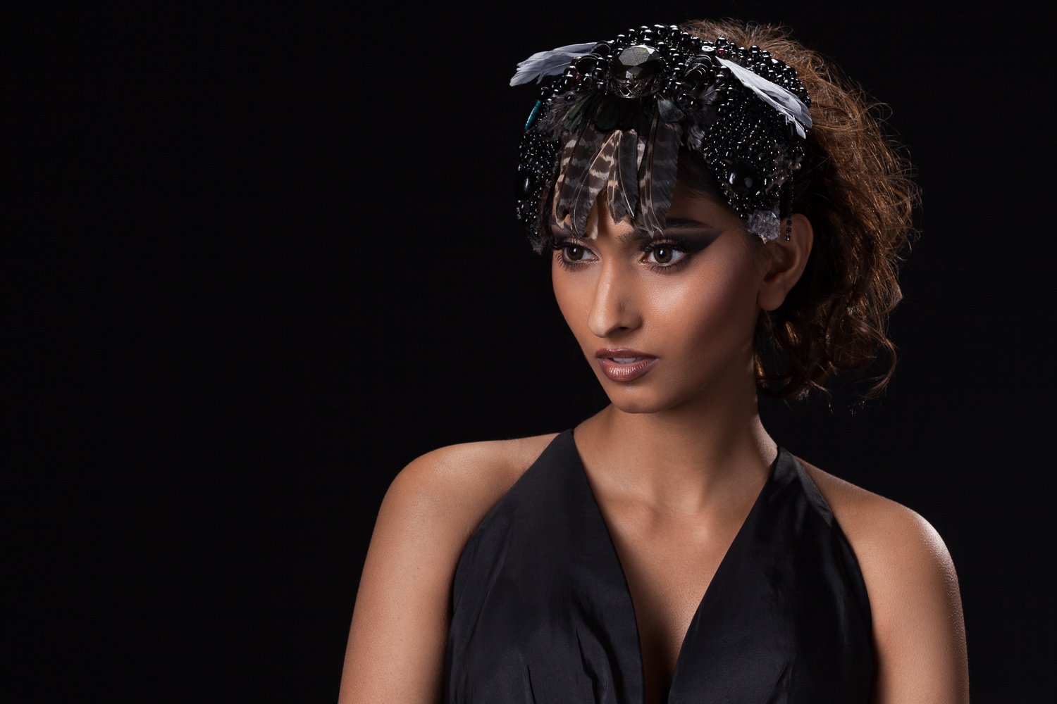 Model in a black beaded headpiece with a jewelled centrepiece and patterned feathers falling across her brow, black halter top, styled and art directed by Laurence Trolet, brand photography