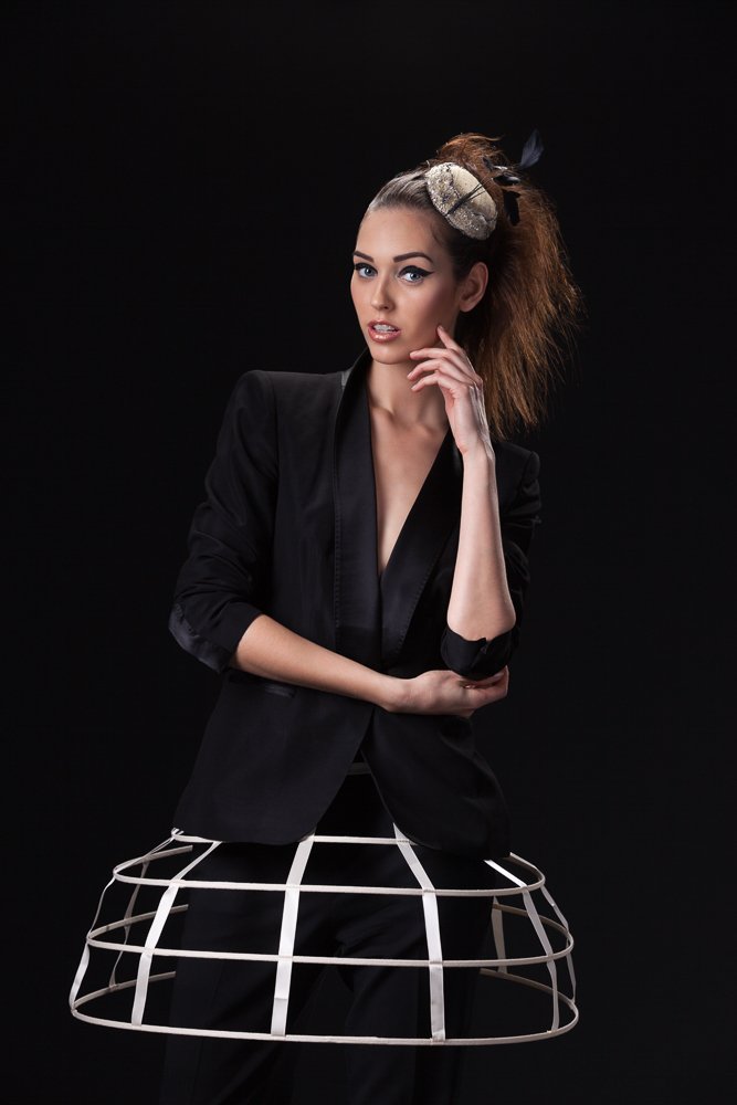 Model in a small headpiece and black tuxedo jacket over a white cage crinoline, hand to her chin, styled and art directed by Laurence Trolet, branding photography