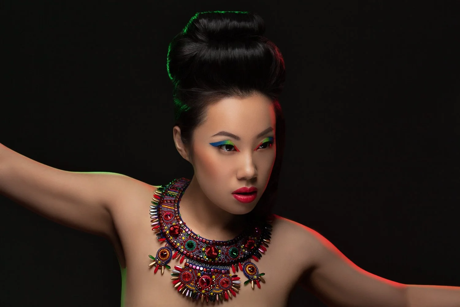 Model with an arm extended in a dynamic pose, wearing an ornate red beaded collar necklace, styled and art directed by Laurence Trolet, brand photography