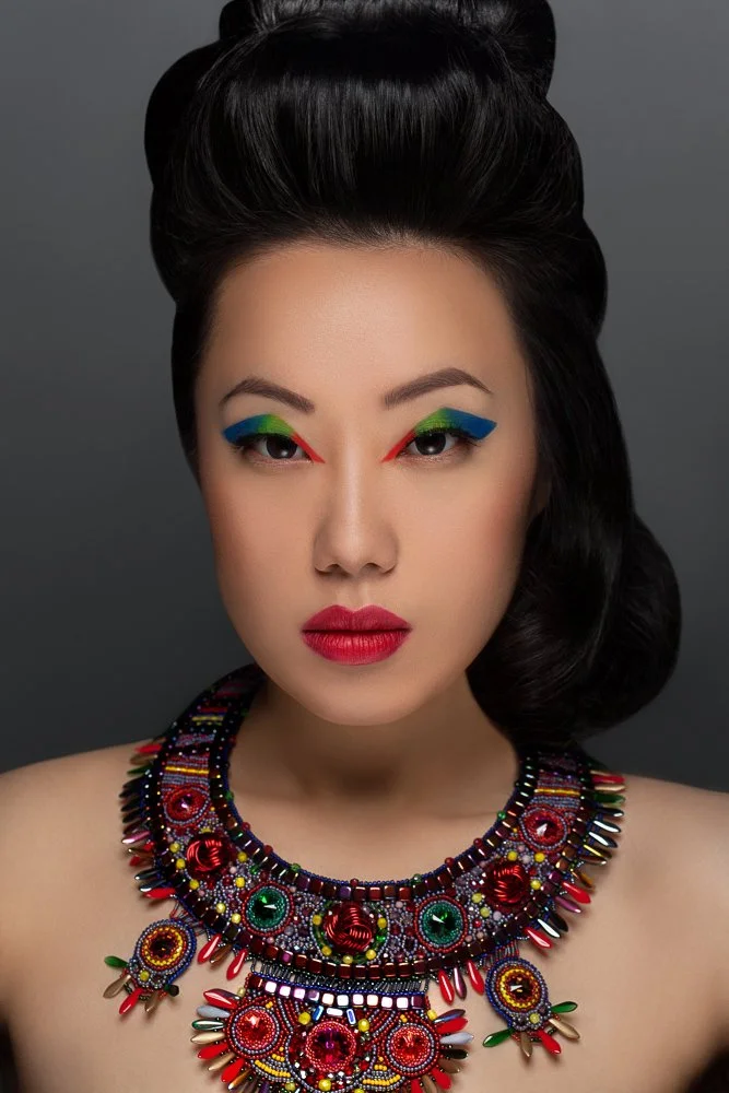 Close-up portrait with a sculpted updo and rainbow eye makeup, ornate beaded collar necklace, styled and art directed by Laurence Trolet, branding photographer