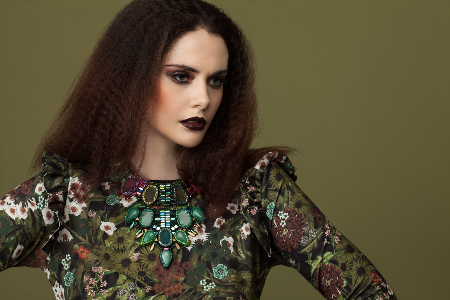 Model with crimped dark hair and plum lips in a floral print top with a jewelled necklace, olive backdrop, styled and art directed by Laurence Trolet, branding photographer