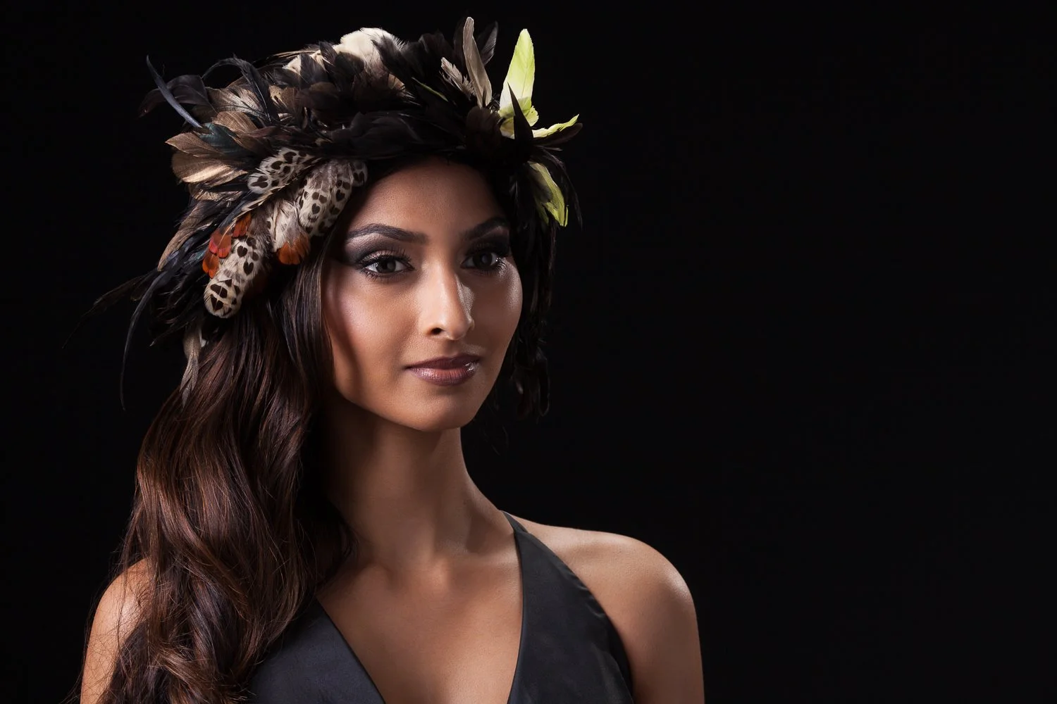 Close-up of a model in a feathered headpiece with patterned and green-tipped feathers, styled and art directed by Laurence Trolet, branding photographer
