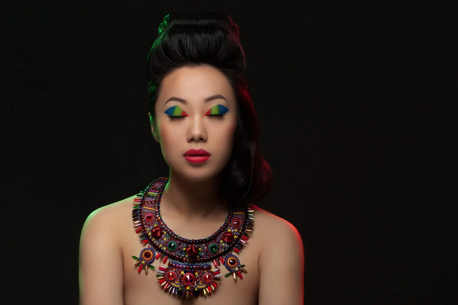 Model with eyes closed and multicoloured eye makeup, wearing an ornate red beaded collar necklace, styled and art directed by Laurence Trolet, brand photography