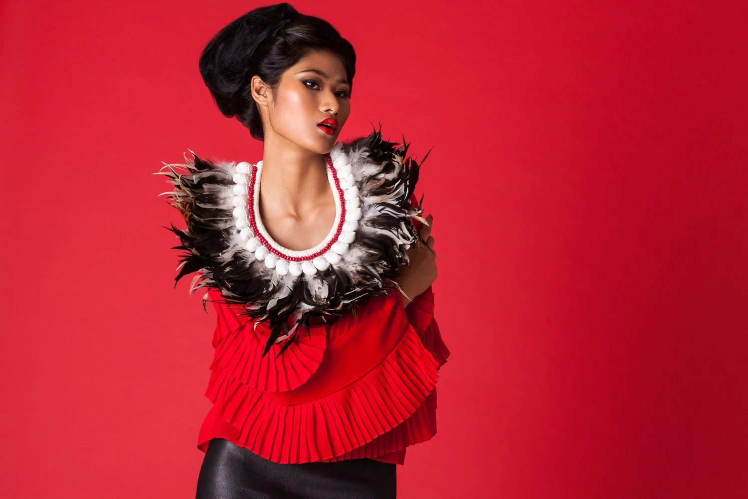 Model against a red backdrop with a red top and feather collar, styled and art directed by Laurence Trolet, fashion photographer