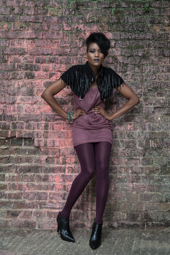 Model in a fringed top and mini dress against a brick wall, styled and art directed by Laurence Trolet, fashion photographer