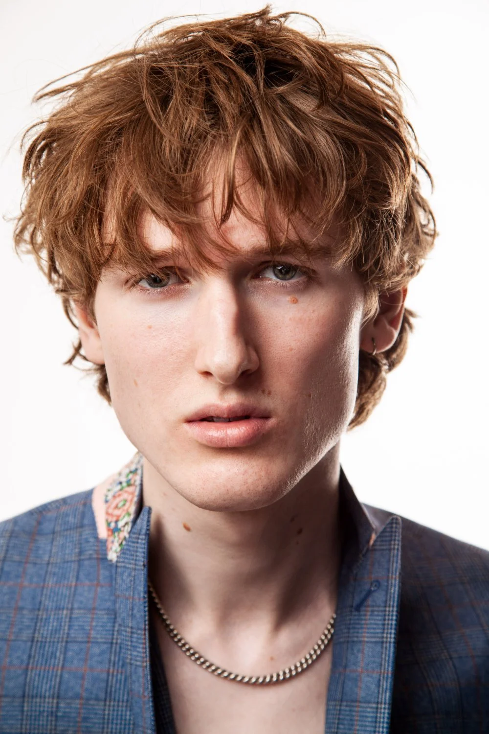 Young man with curly ginger hair, blue jacket, headshot against a plain background