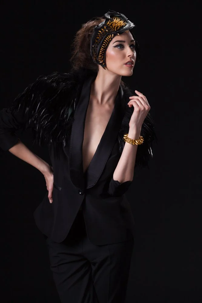 Model in a gold and black feathered headpiece, black feather cape and tuxedo jacket, styled and art directed by Laurence Trolet, branding photography