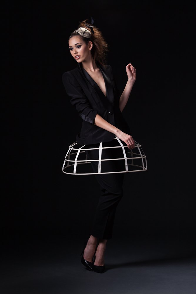 Full-length portrait of a model in a small headpiece, black suit and white cage crinoline, styled and art directed by Laurence Trolet, brand photographer