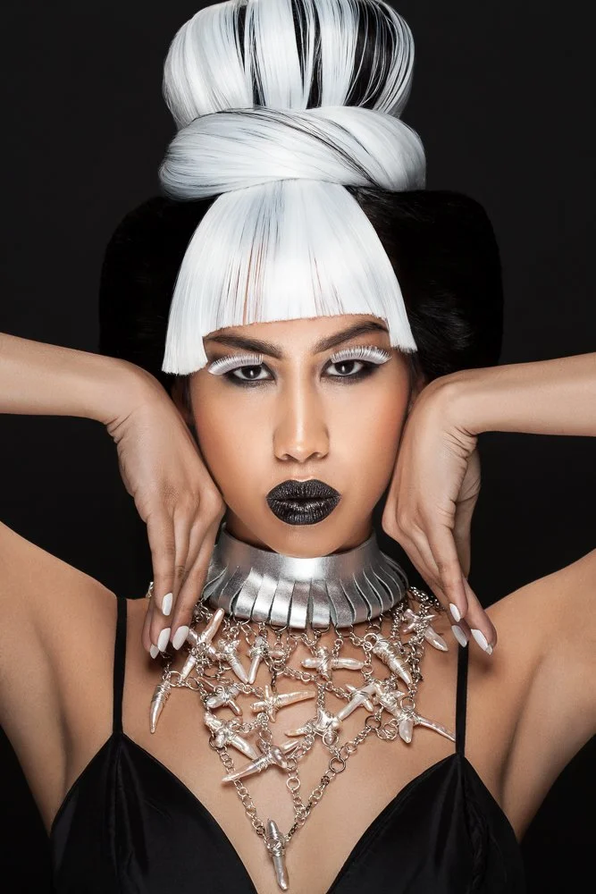 Model framing her face with her hands, wearing a silver collar and statement necklace, styled and art directed by Laurence Trolet, brand photography