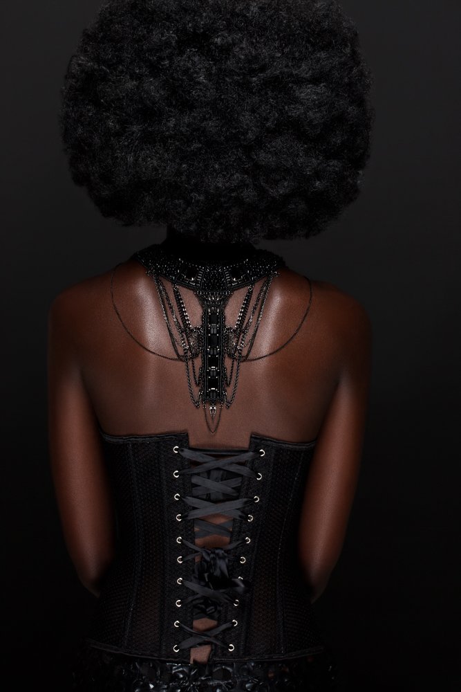 Back view of a model in a laced black corset, black chain necklace falling down her back, styled and art directed by Laurence Trolet, brand photographer