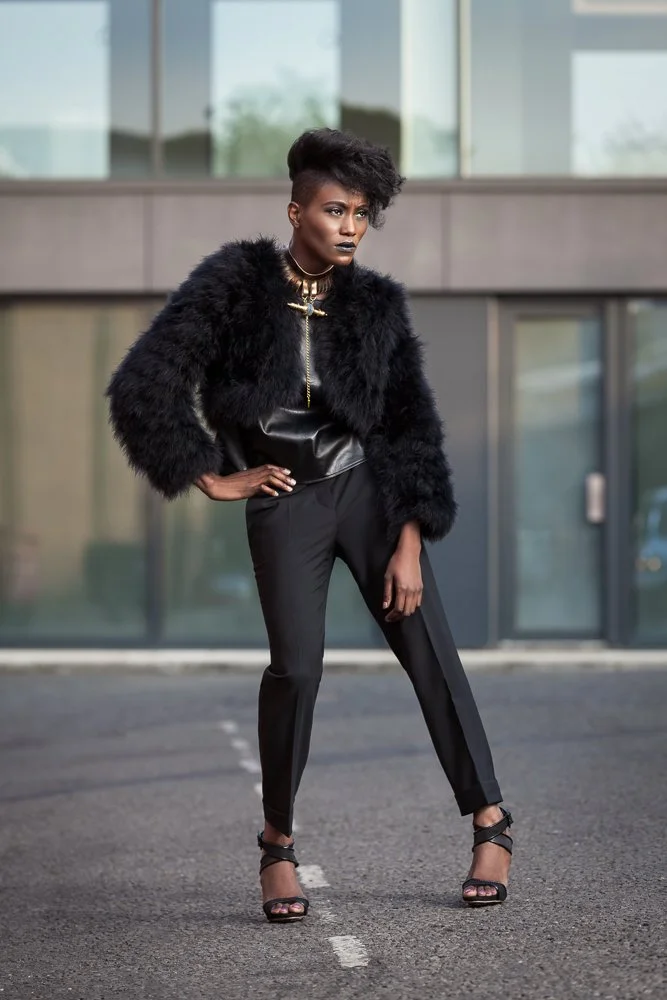 Model in a faux fur jacket and black trousers, urban exterior setting, styled and art directed by Laurence Trolet, editorial fashion photography
