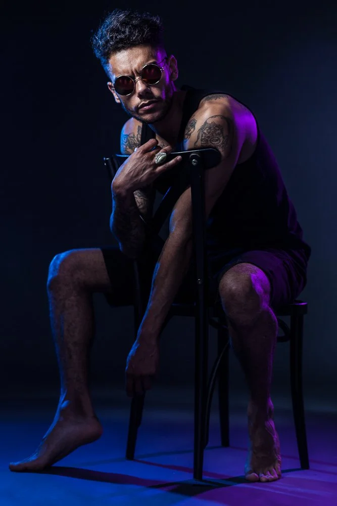 Male model with tattoos seated under blue lighting, styled and art directed by Laurence Trolet, editorial fashion photography