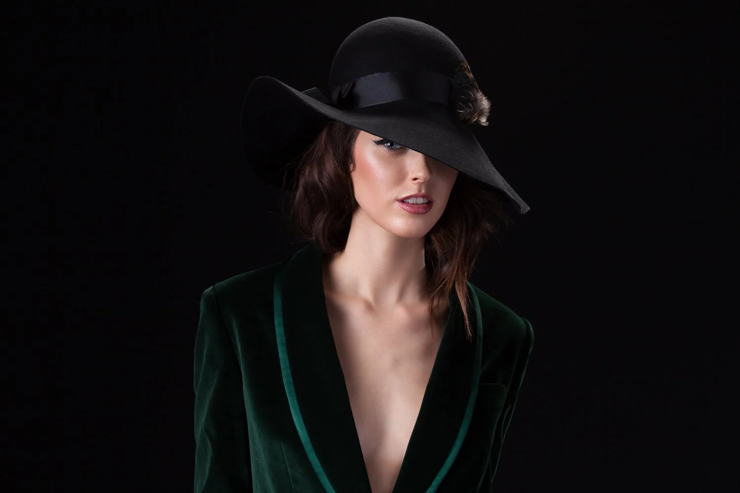 Model in a black wide-brim hat and green velvet jacket against a dark backdrop, styled and art directed by Laurence Trolet, branding photography