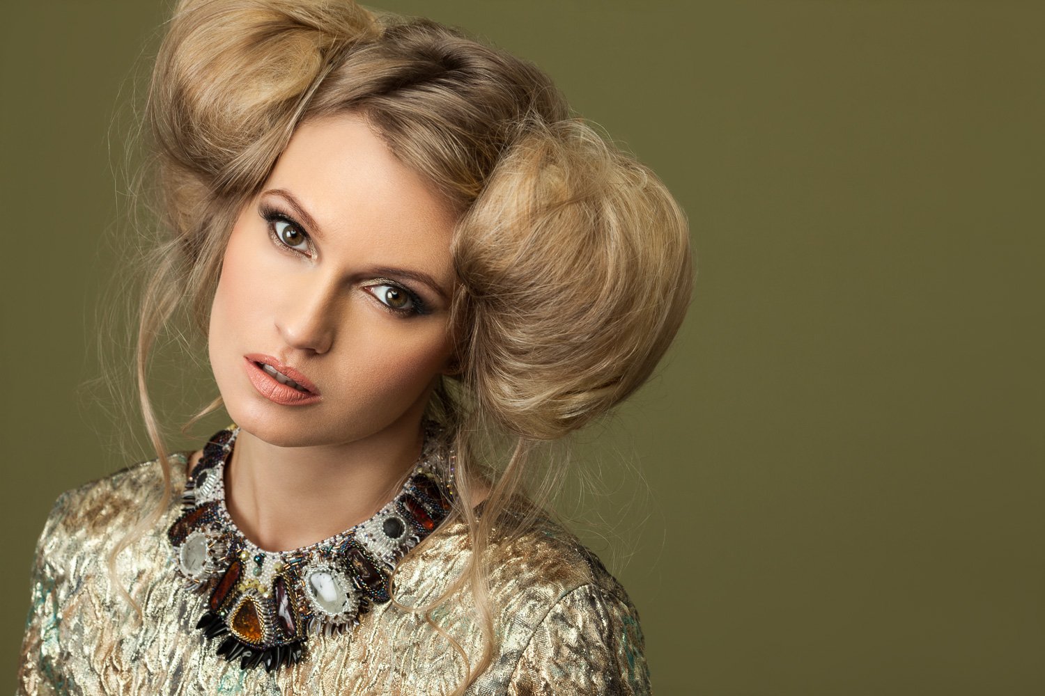 Close-up of a model with sculpted blonde curls, wearing a jewelled statement necklace, olive backdrop, styled and art directed by Laurence Trolet, brand photography