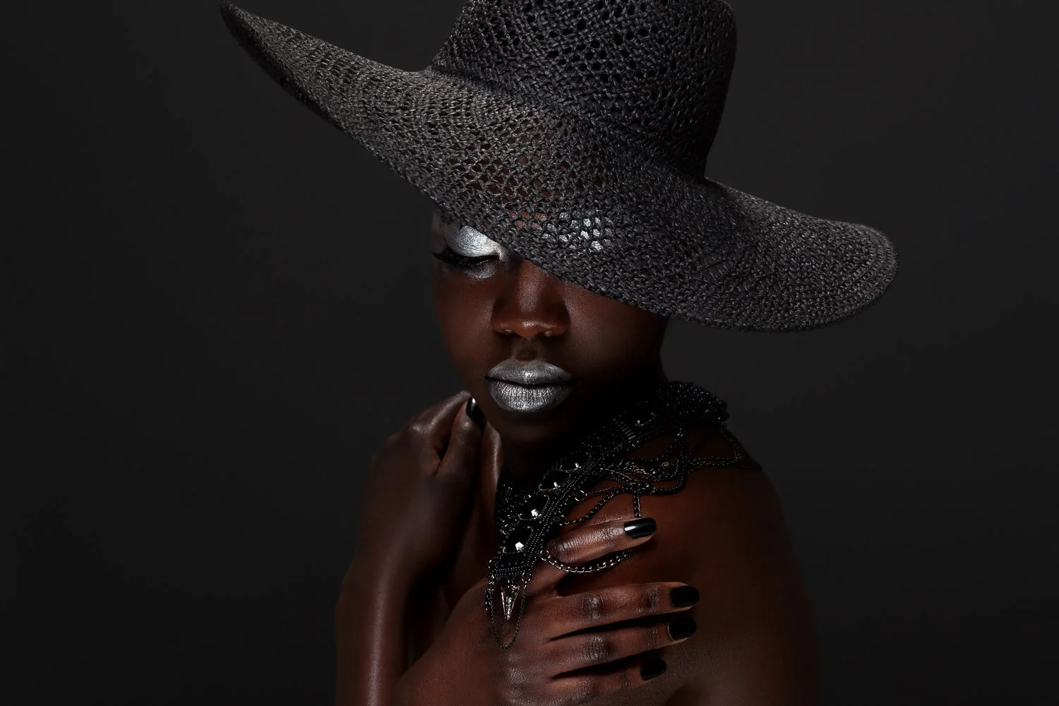 Model in a black wide-brim woven hat with silver lips and a black beaded necklace, styled and art directed by Laurence Trolet, branding photography