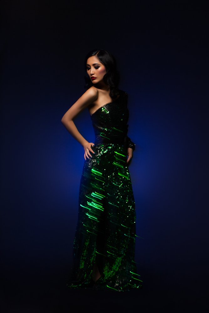 Model in a green sequin gown, standing pose against a deep blue backdrop, styled and art directed by Laurence Trolet, editorial photography
