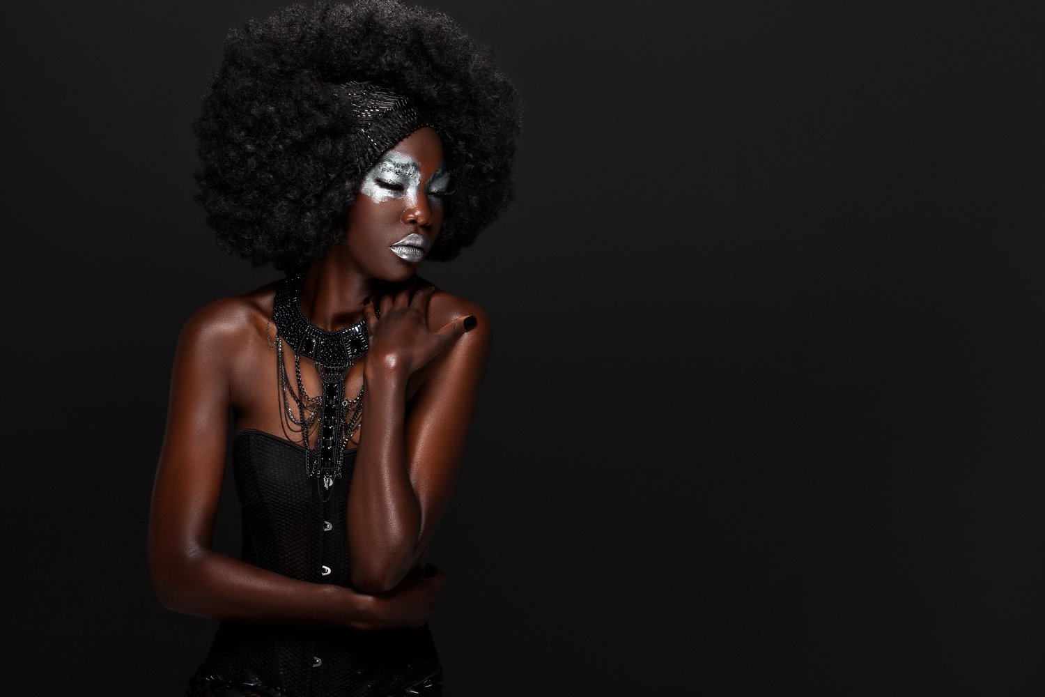 Model with a voluminous afro and silver eye makeup, wearing a layered black chain necklace, styled and art directed by Laurence Trolet, branding photographer