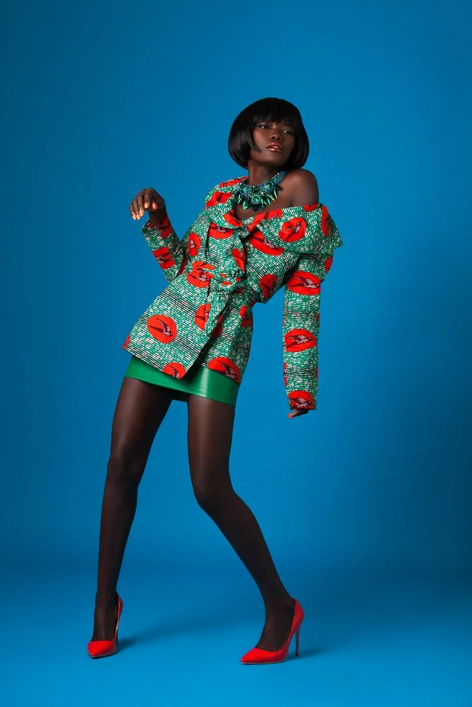 Model in an African wax print jacket and mini skirt against a blue backdrop, styled and art directed by Laurence Trolet, fashion photographer