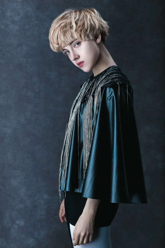 Model with short blonde hair in a draped cape, moody lighting, fashion photographer