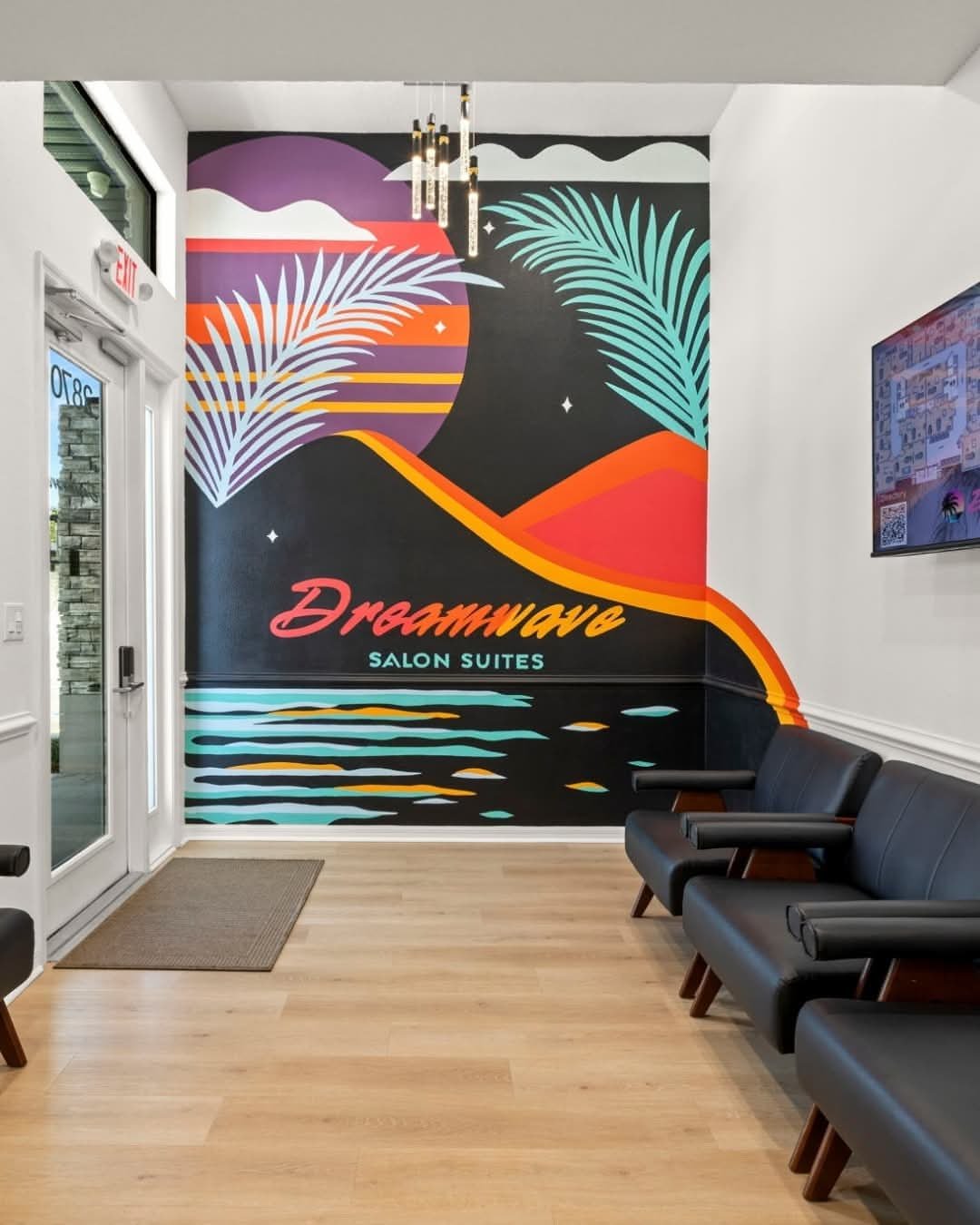 Colorful mural at Dreamwave Salon Suites with palm trees, mountains, and a sunset, featuring water and the salon's name.