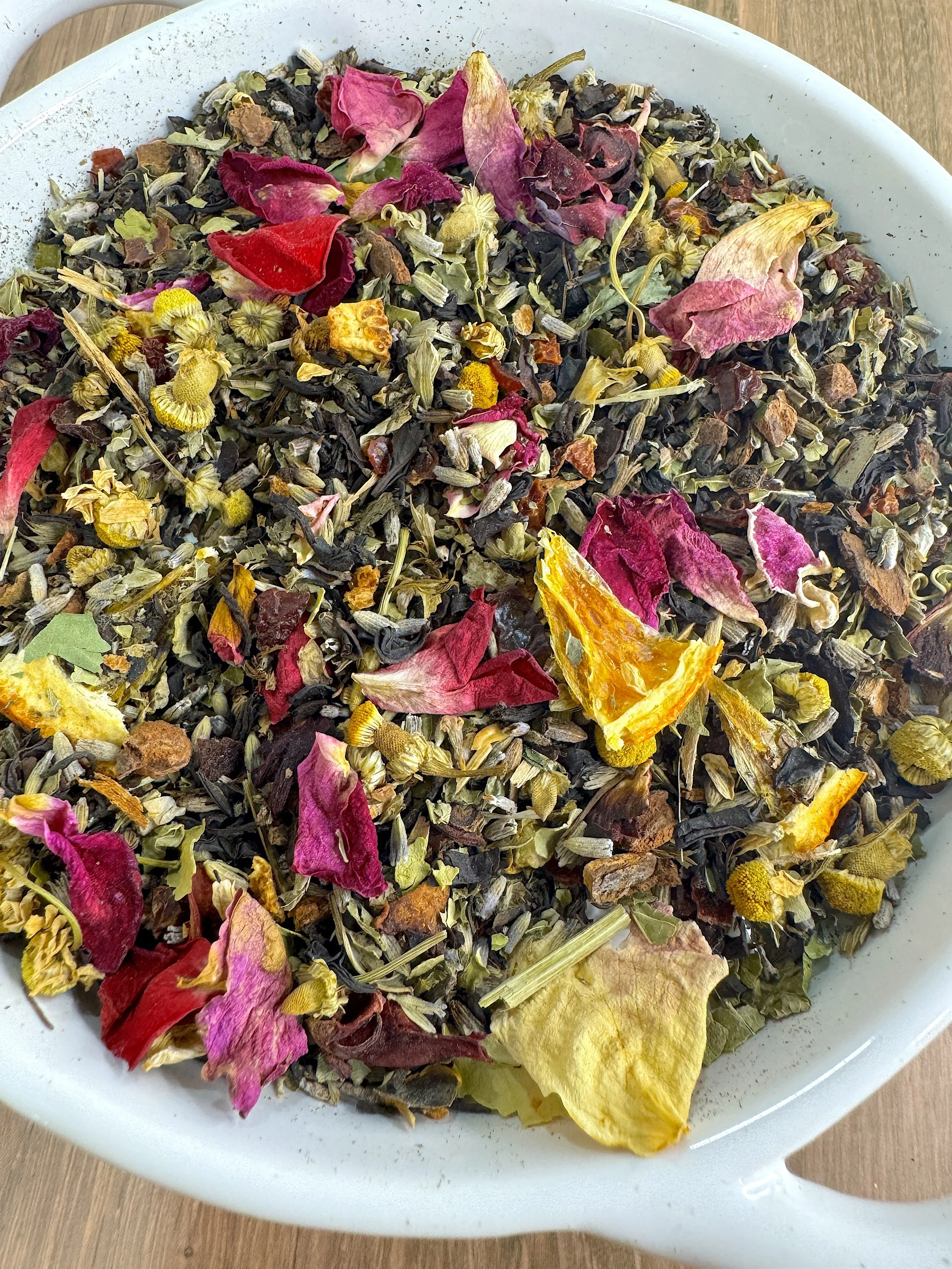 A bag of Annapelle's Table's SereniTea tea blend with loose herbs visible and dried orange slices and flowers nearby