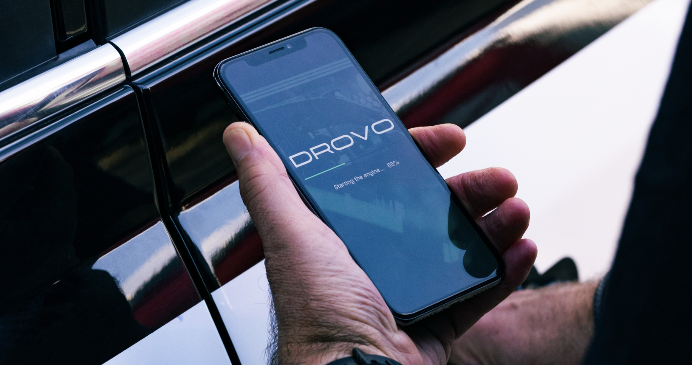 A person holding a smartphone with the screen displaying the logo and status of the Dromo app, showing the process of starting the engine.