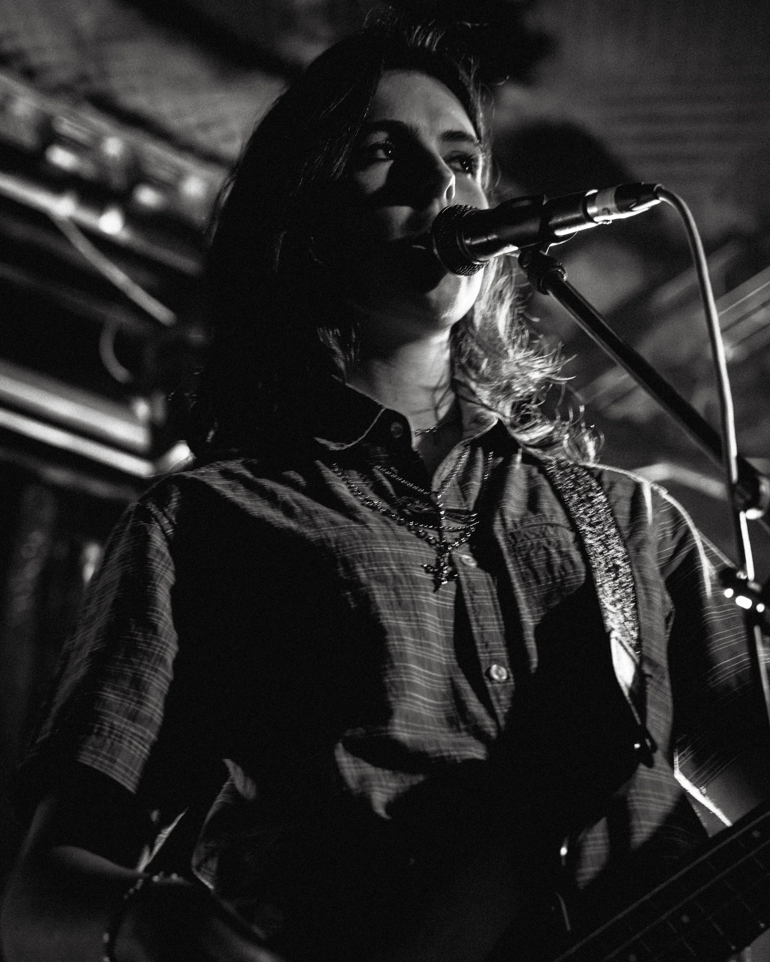 A woman singing into a microphone while playing a guitar, in a dimly lit environment.