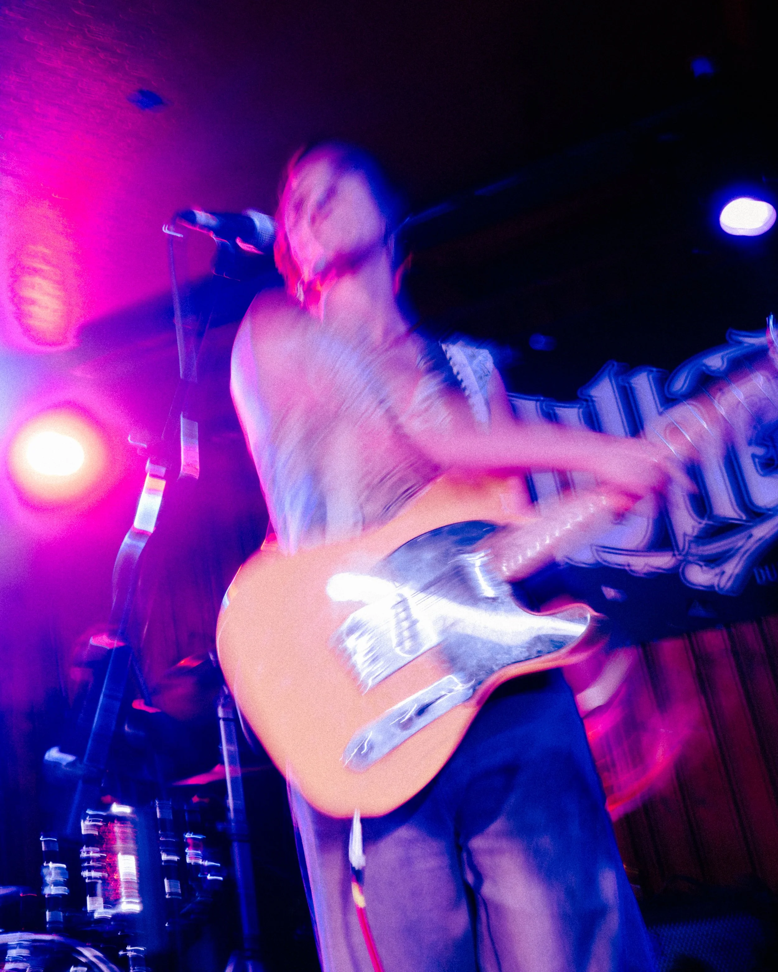 A blurry person playing an electric guitar on a stage with colorful, neon lighting.