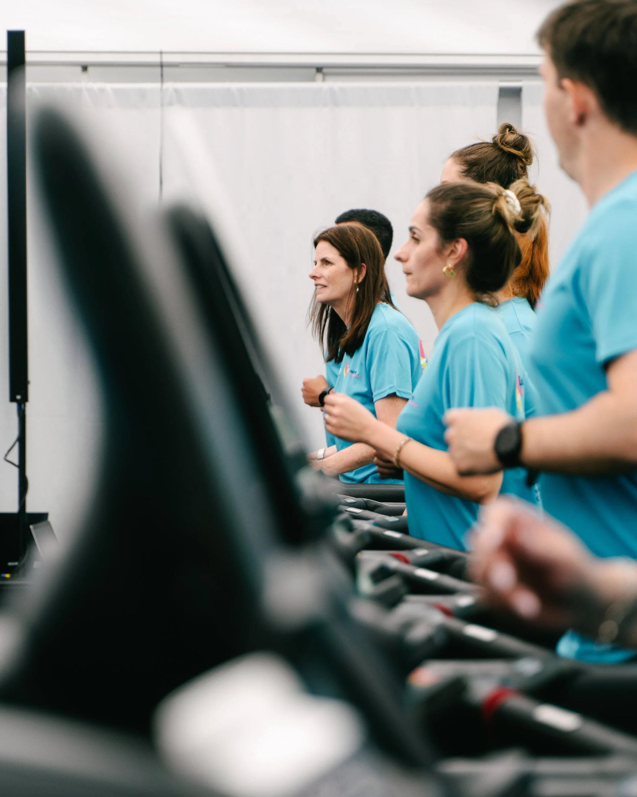 Side view of a group of women in blue shirts running on treadmills in a gym or fitness center.