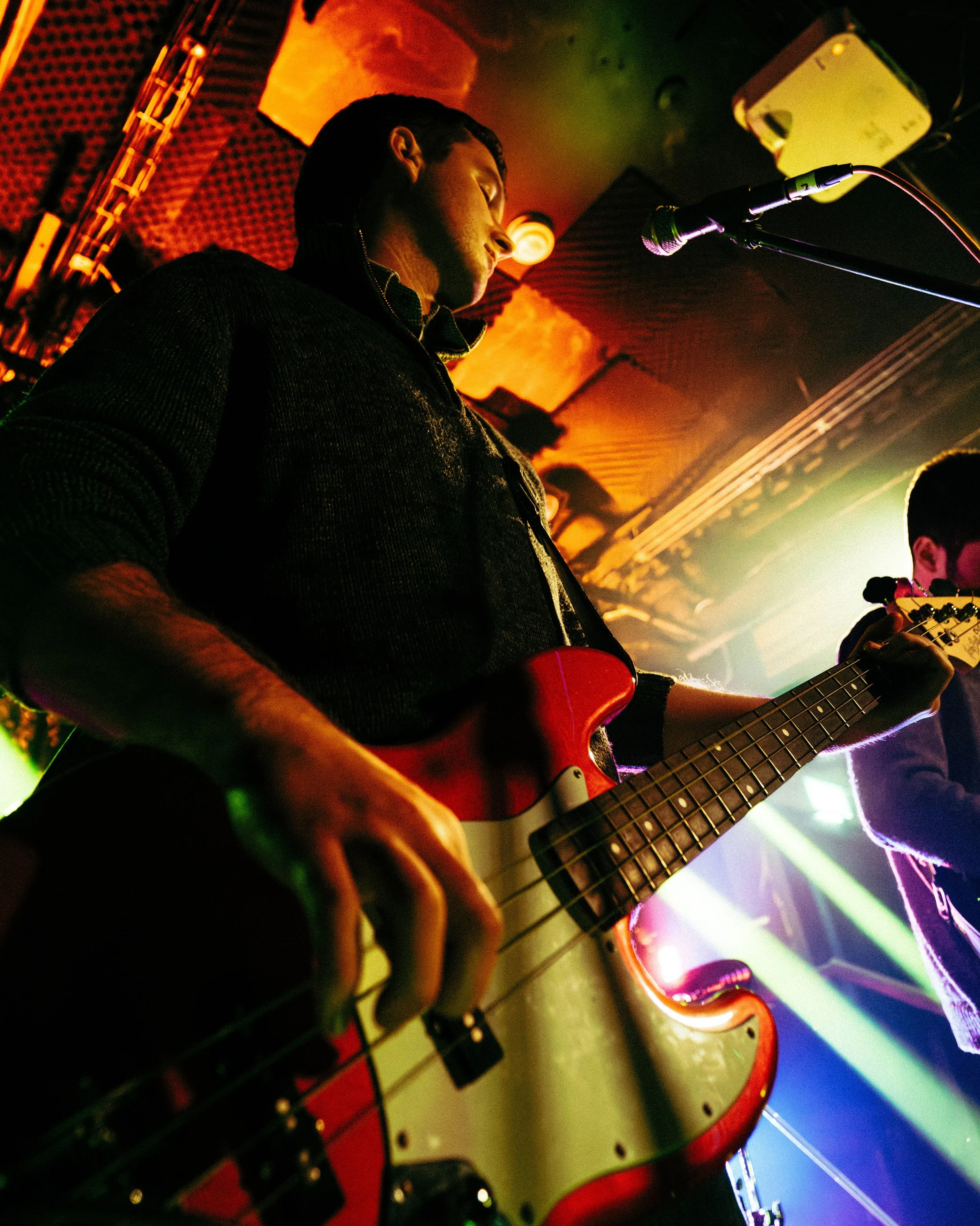 A musician playing a red electric guitar on stage with colorful lighting.