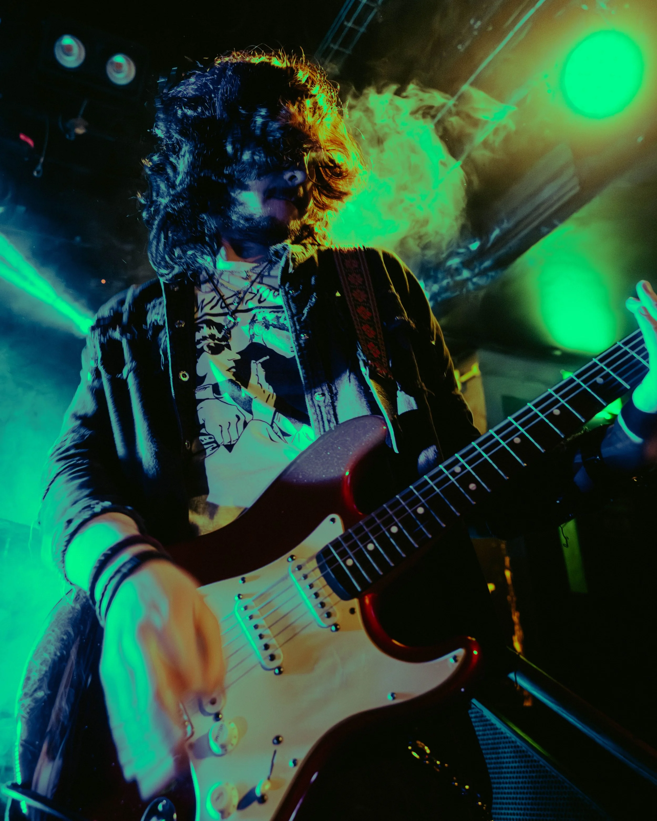 A musician playing an electric guitar on stage with colorful stage lights and smoke.