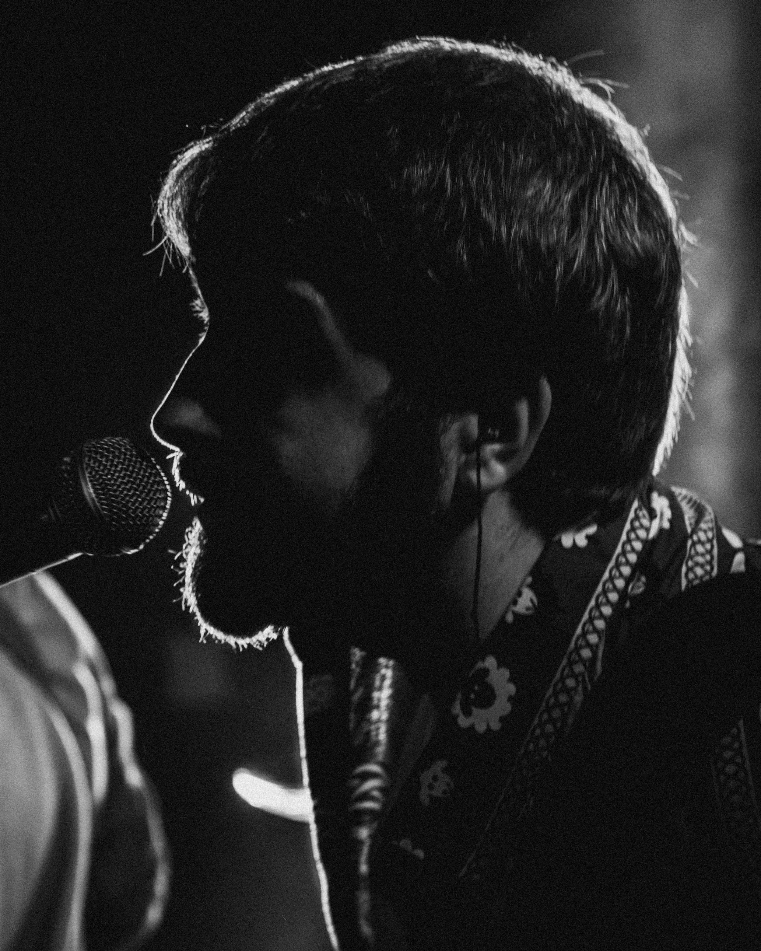 Silhouette of a young artist singing into a microphone with headphones, backlit and in black and white.
