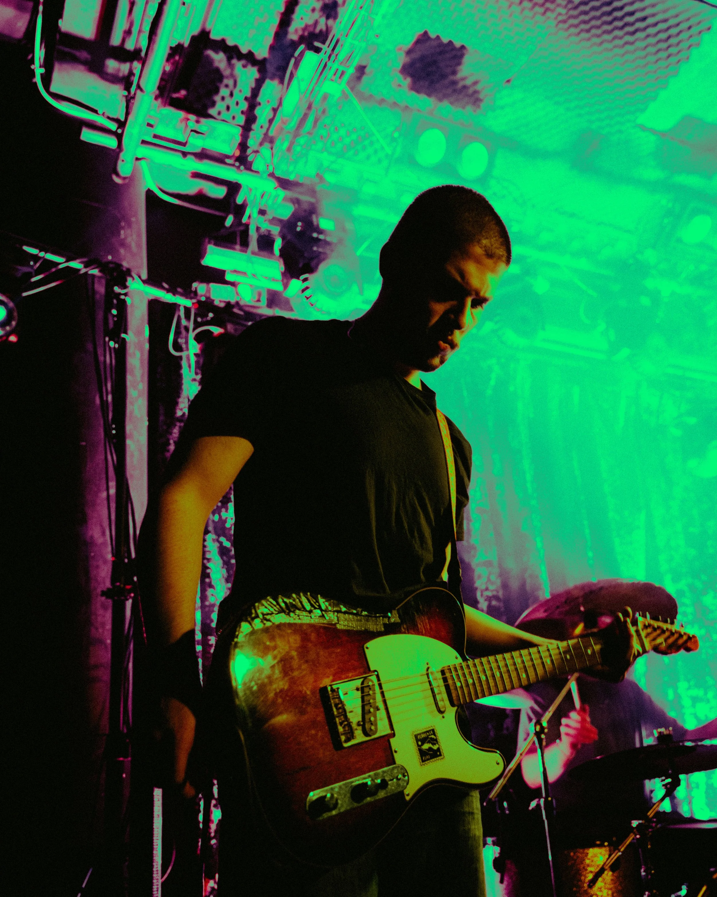 A person playing an electric guitar on stage under colorful lights with a band in the background.