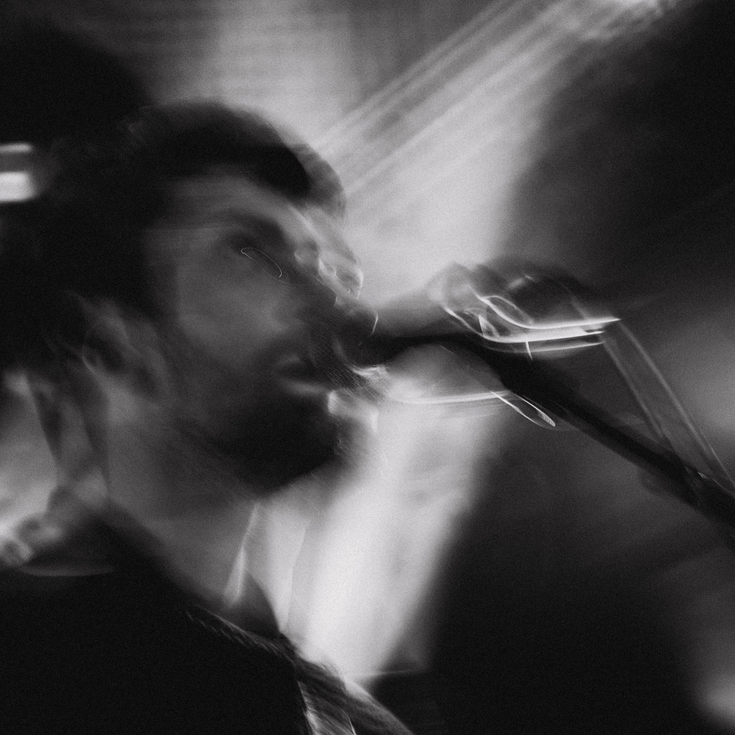 A blurry black and white photo of a man with glasses singing into a microphone.