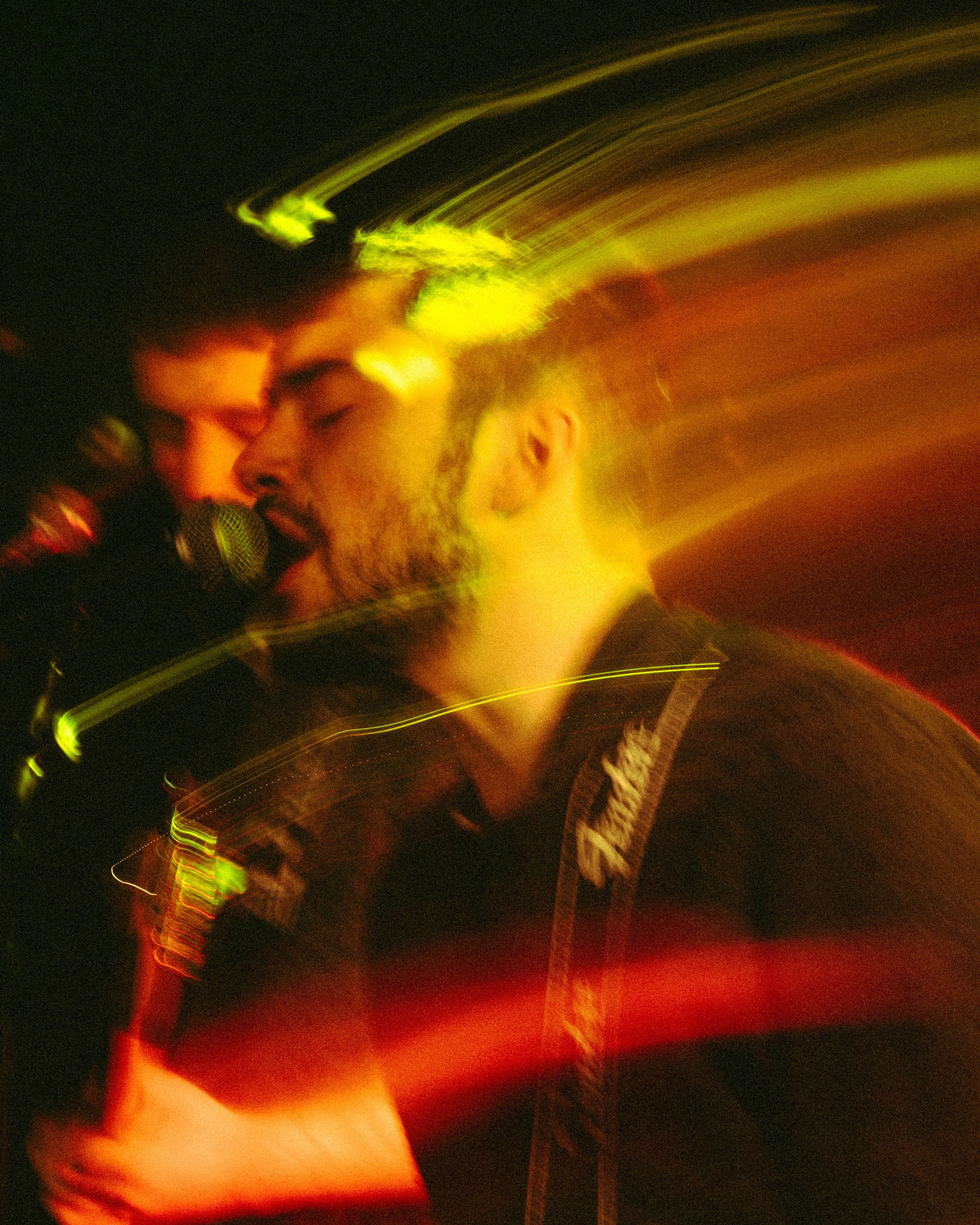 A man singing into a microphone with colorful light trails creating a motion blur effect.