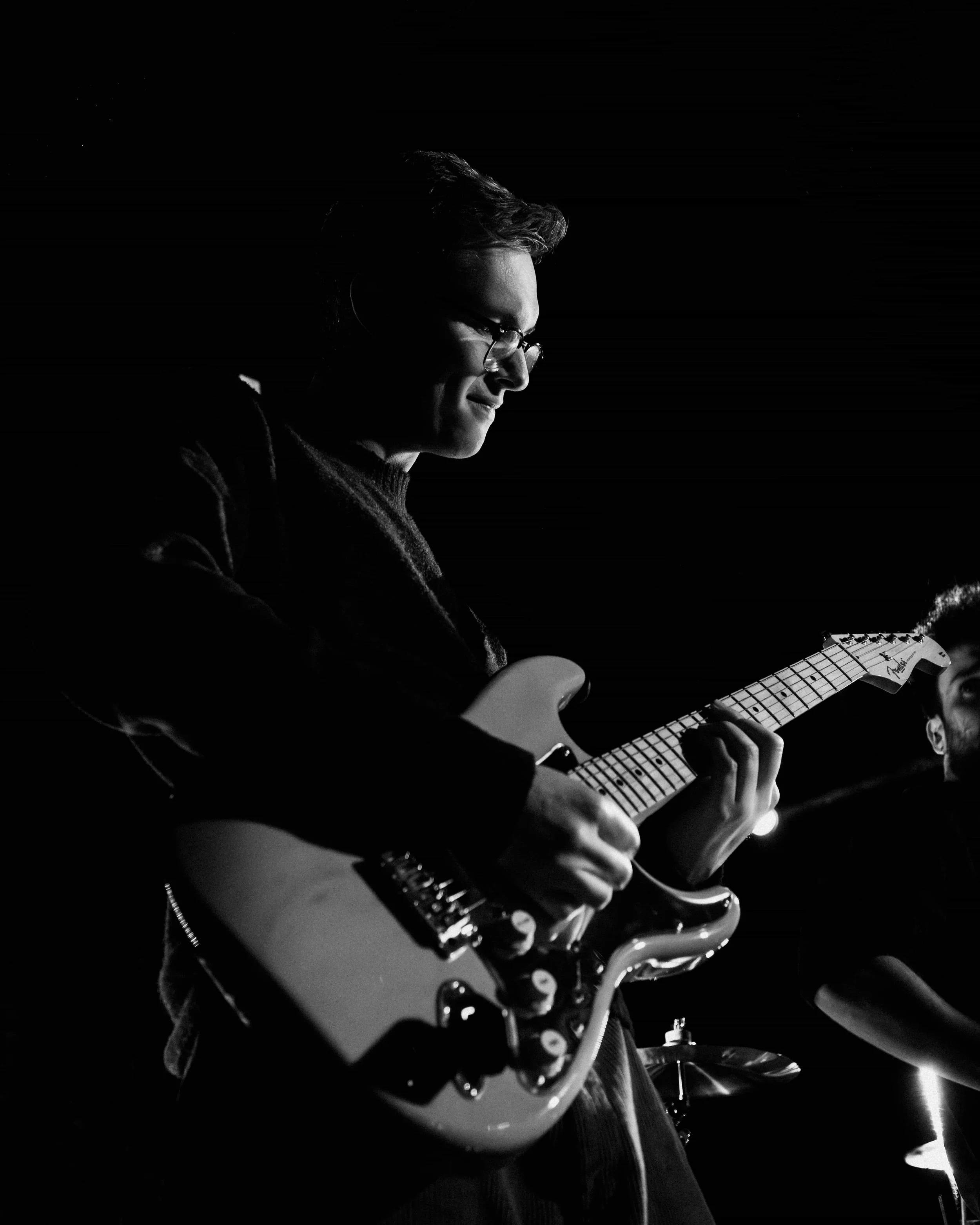 A person playing an electric guitar on stage, with a dark background, in black and white