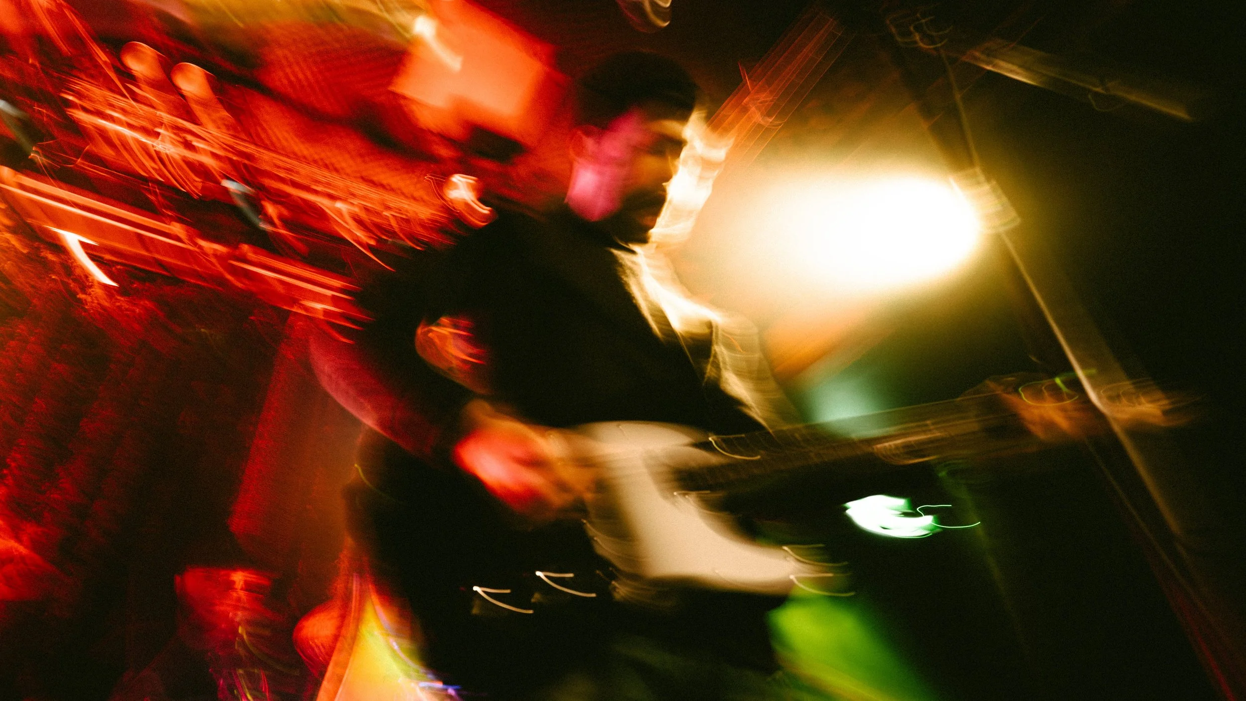Blurred image of a musician playing an electric guitar on stage, with colorful stage lights creating a dynamic atmosphere.