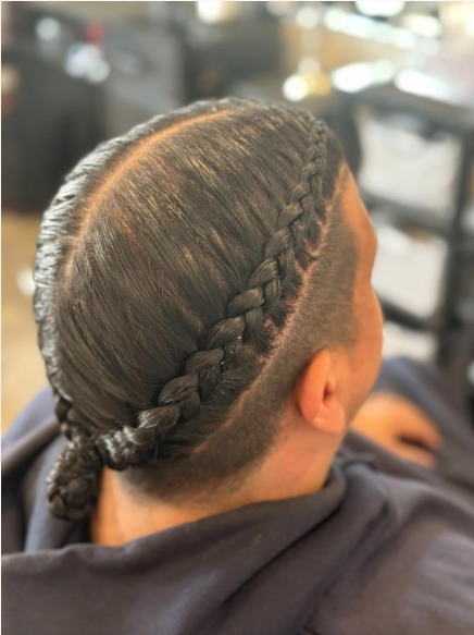Person with dark, shiny hair styled in a French braid with a fade on the sides.
