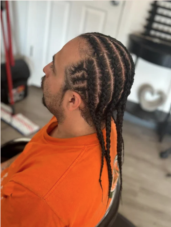Man with braided hairstyle sitting in a chair indoors.