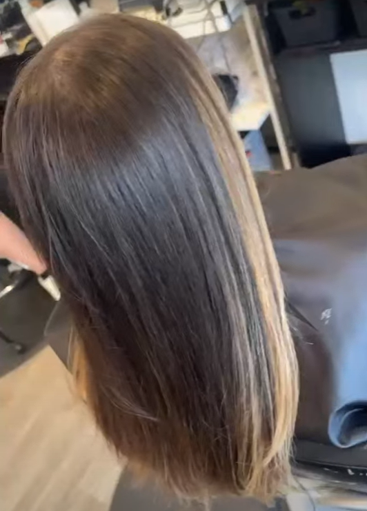 Back of a person's head with long, straight, brown hair in a hair salon