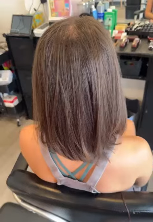 Back of a woman with shoulder-length straight brown hair in a salon chair.