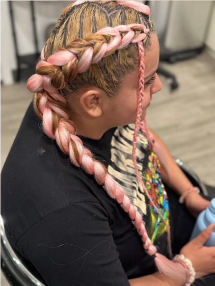 Woman with long, pink-dyed hair styled in a large braid, sitting in a wheelchair.