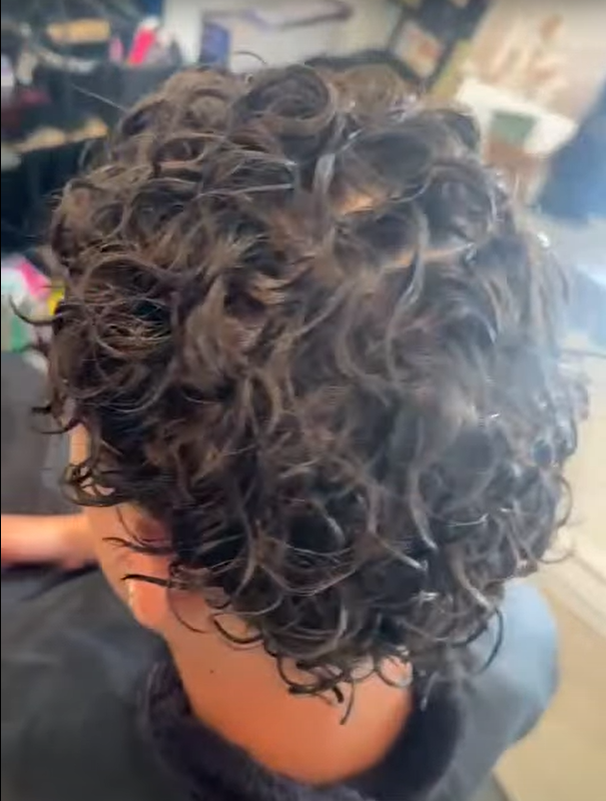 Back view of a person with short, dark, curly hair.