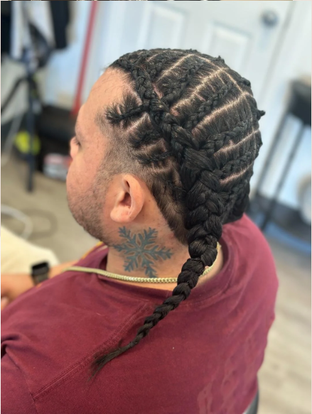 A person with long braided hair and a neck tattoo sitting indoors.