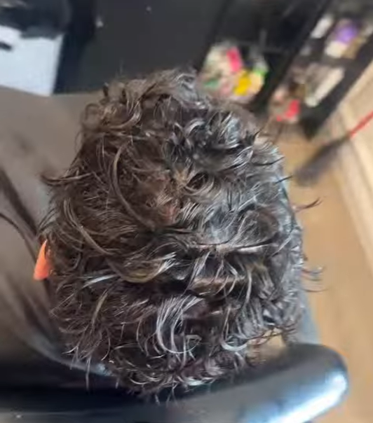 Top-down view of a person with curly dark hair in a salon or barbershop setting.