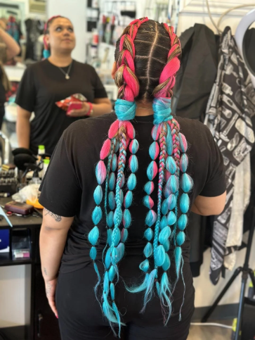 Back view of a woman with long, colorful braided hair in pink, blue, and blonde, in a store.