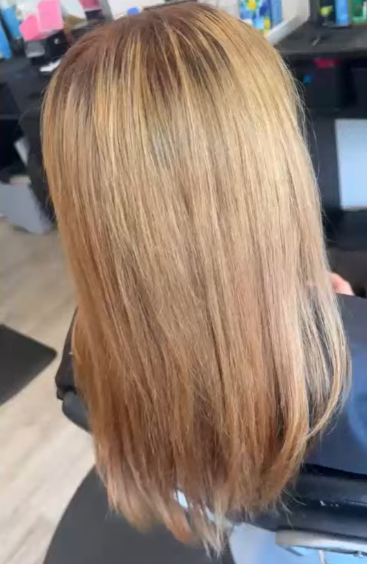 Back view of a woman with straight, shoulder-length blonde hair at a hair salon.