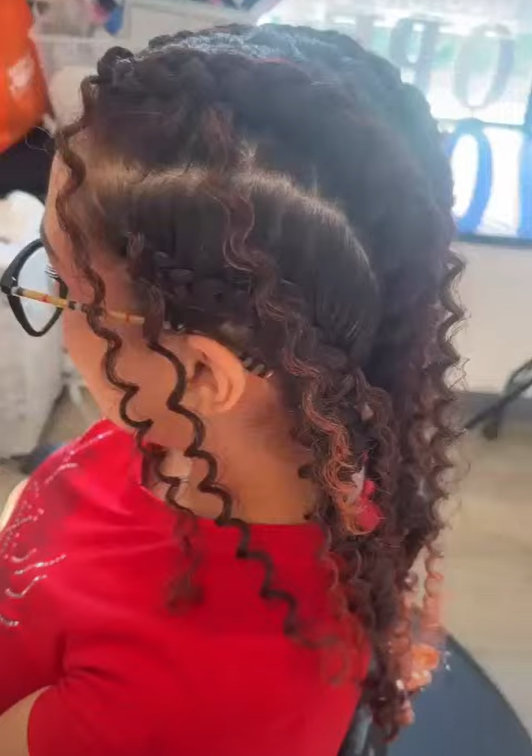 A woman with curly hair styled in two layers, with the top layer pinned back, wearing glasses and a red shirt.