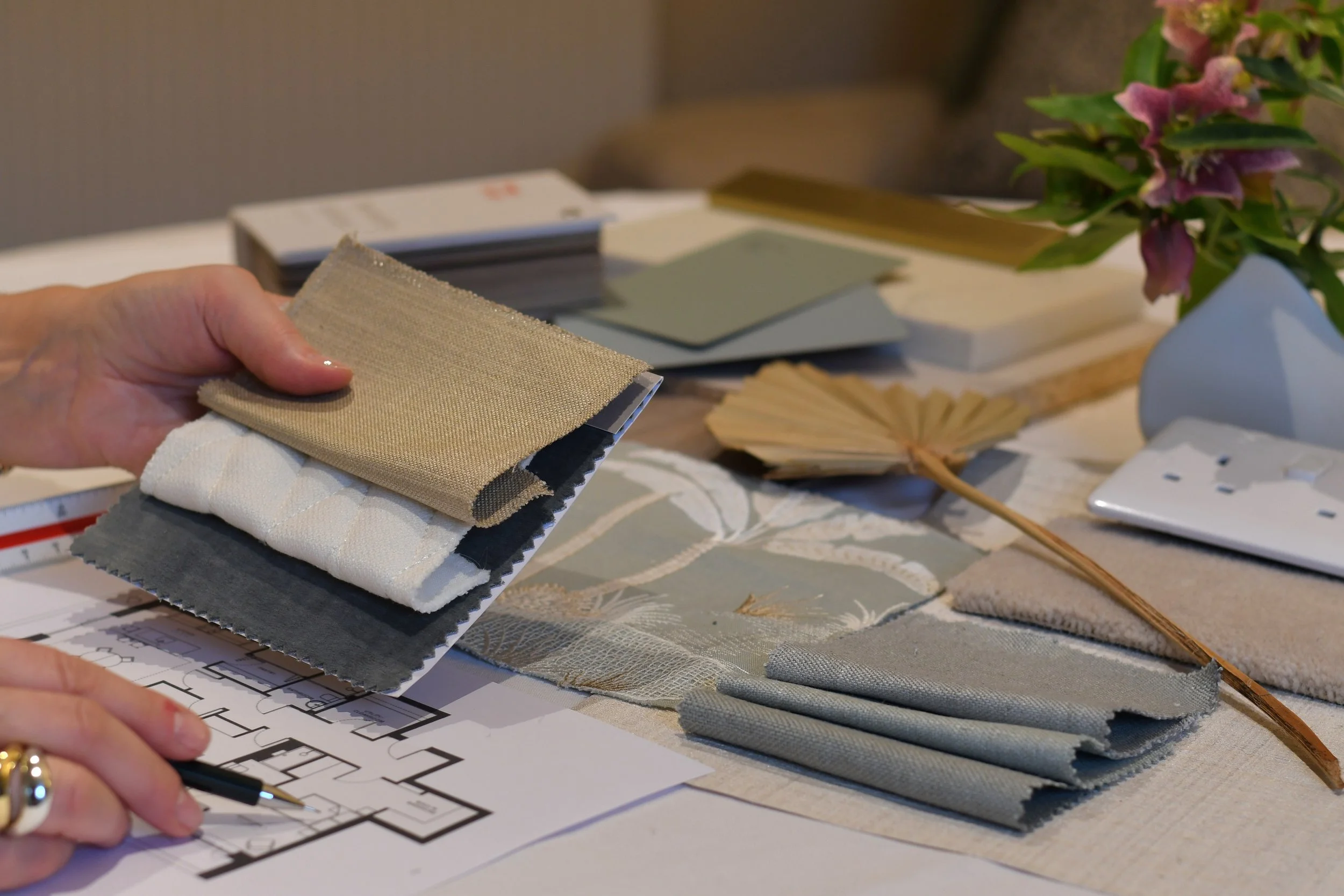 A selection of materials samples assembled by Bobby Lardner, interior designer,in teal and green tones for a Guest WC scheme - open catalog displaying bathroom fixtures, swatches of paint, wallpaper and brass samples, against a beige background.